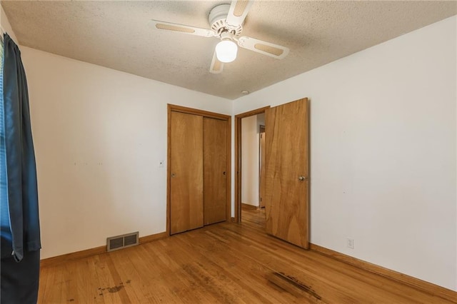 unfurnished bedroom with a textured ceiling, a closet, light wood finished floors, and visible vents
