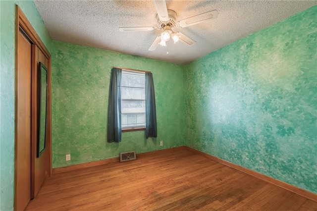 empty room with visible vents, light wood-style flooring, ceiling fan, and a textured ceiling