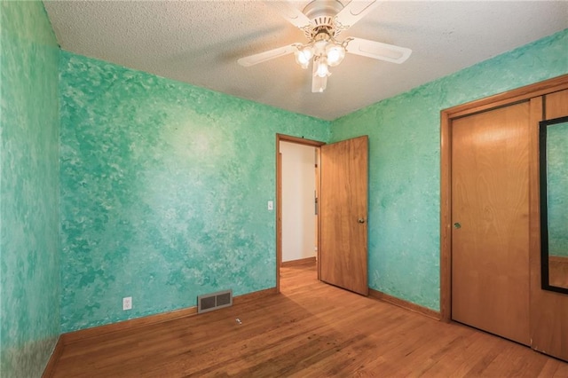unfurnished bedroom featuring a closet, visible vents, baseboards, ceiling fan, and wood finished floors