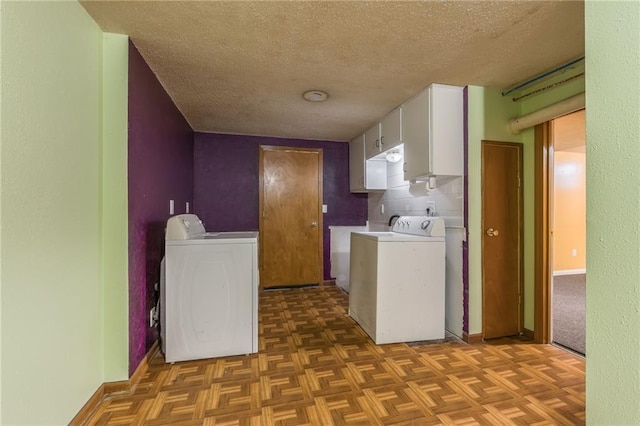clothes washing area featuring baseboards, washing machine and clothes dryer, cabinet space, and a textured ceiling