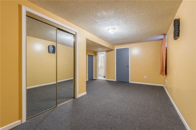 unfurnished bedroom featuring baseboards, a textured ceiling, a closet, and dark colored carpet
