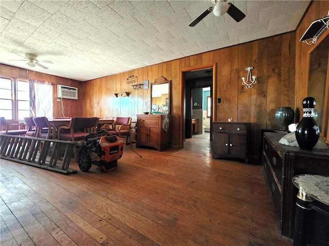 living room featuring wooden walls, wood-type flooring, ceiling fan, and an AC wall unit