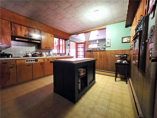 kitchen featuring gas cooktop, a baseboard heating unit, wood walls, wainscoting, and light floors