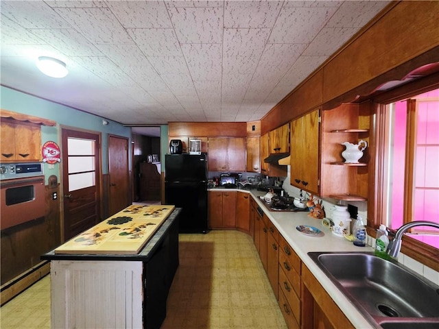 kitchen featuring light floors, a sink, freestanding refrigerator, and brown cabinets