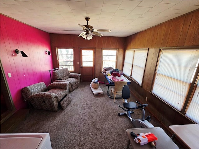 exercise area with wood walls, carpet flooring, and a ceiling fan