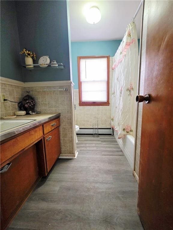 full bathroom with a baseboard radiator, toilet, a wainscoted wall, wood finished floors, and tile walls