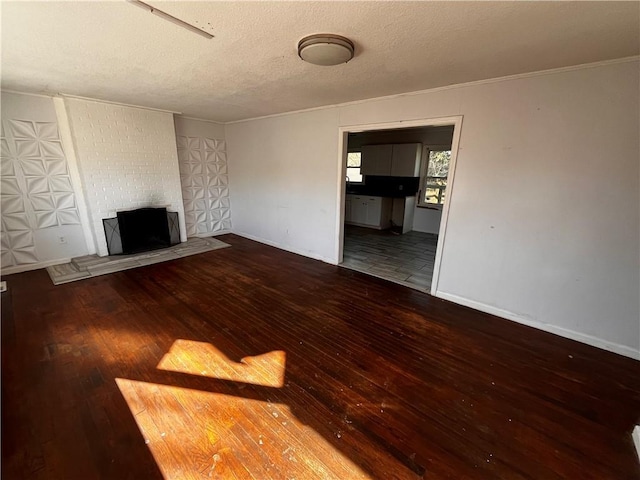 unfurnished living room with a brick fireplace, a textured ceiling, baseboards, and hardwood / wood-style flooring