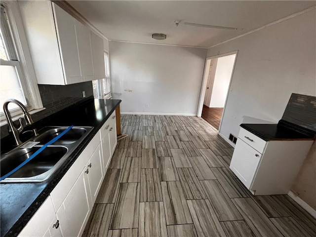 kitchen with white cabinets, dark countertops, a sink, wood tiled floor, and backsplash