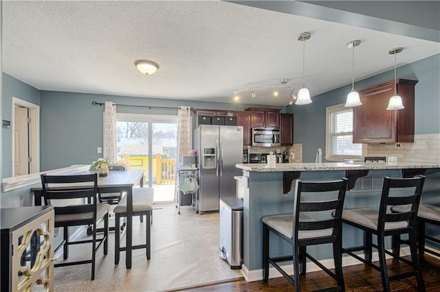 kitchen with stainless steel appliances, a peninsula, backsplash, and a kitchen breakfast bar