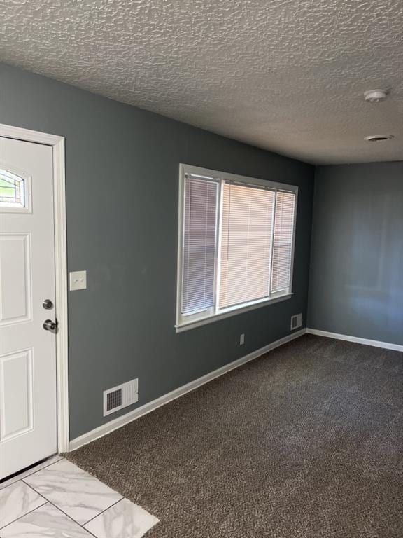 foyer entrance featuring a textured ceiling, carpet floors, visible vents, and baseboards