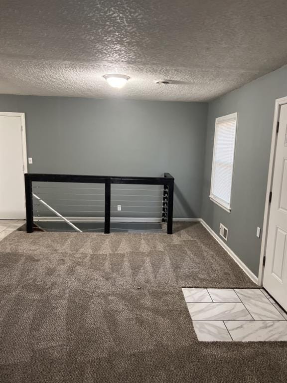 empty room featuring a textured ceiling, carpet flooring, visible vents, and baseboards