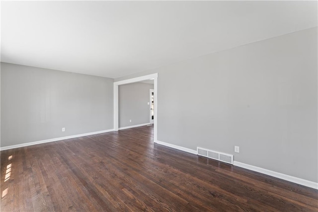 empty room with dark wood-style flooring, visible vents, and baseboards