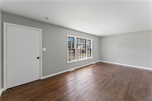 spare room with dark wood-style floors, visible vents, and baseboards