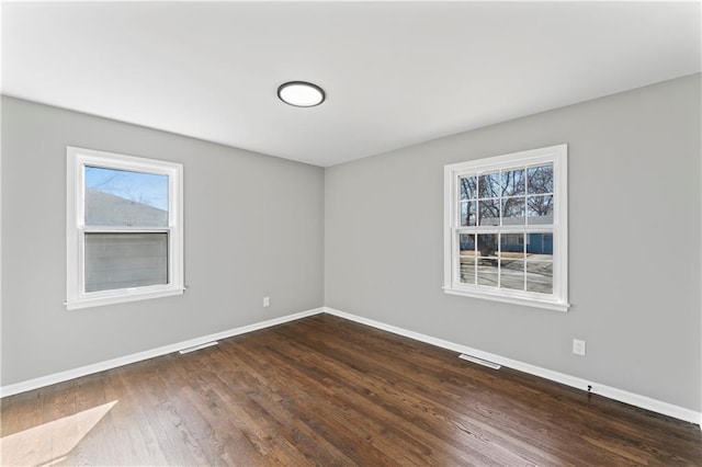 unfurnished room with dark wood-type flooring, visible vents, and baseboards