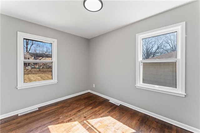 empty room featuring dark wood finished floors, visible vents, and baseboards