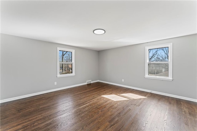 empty room with dark wood-type flooring, visible vents, and baseboards