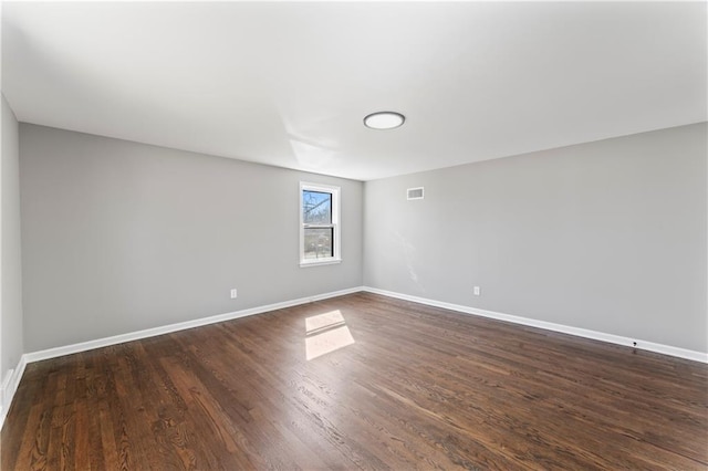 empty room featuring dark wood-style flooring, visible vents, and baseboards