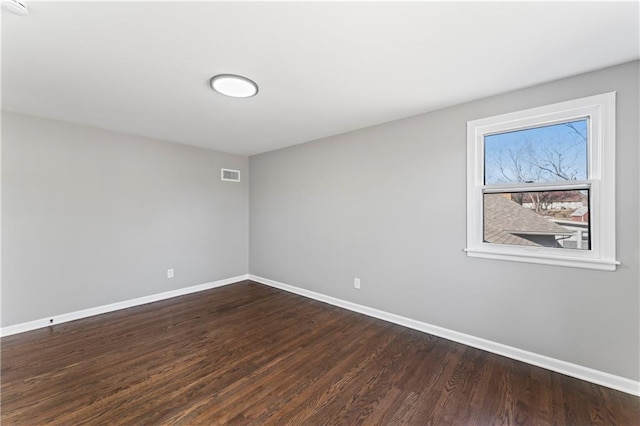 empty room featuring dark wood-style flooring, visible vents, and baseboards