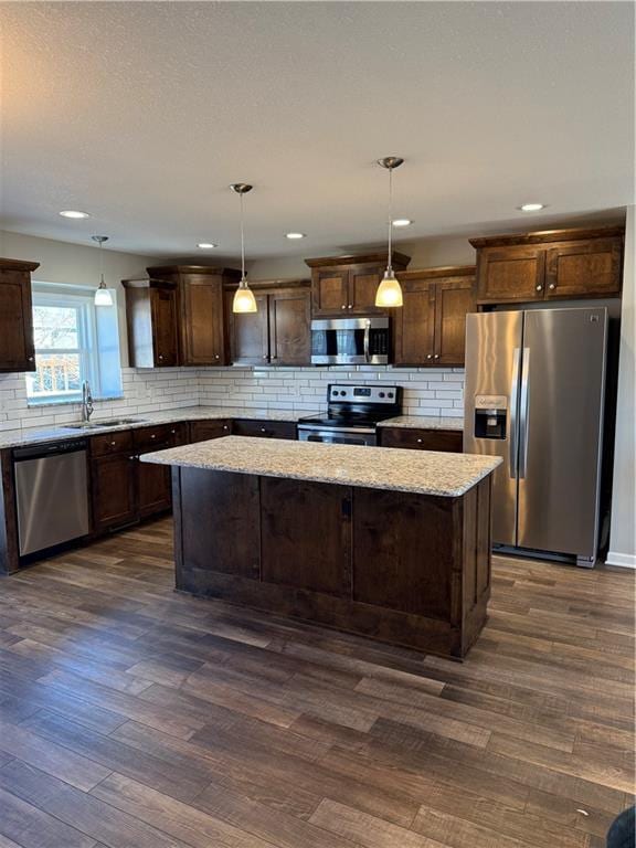 kitchen featuring dark brown cabinetry, dark wood-type flooring, appliances with stainless steel finishes, a center island, and tasteful backsplash