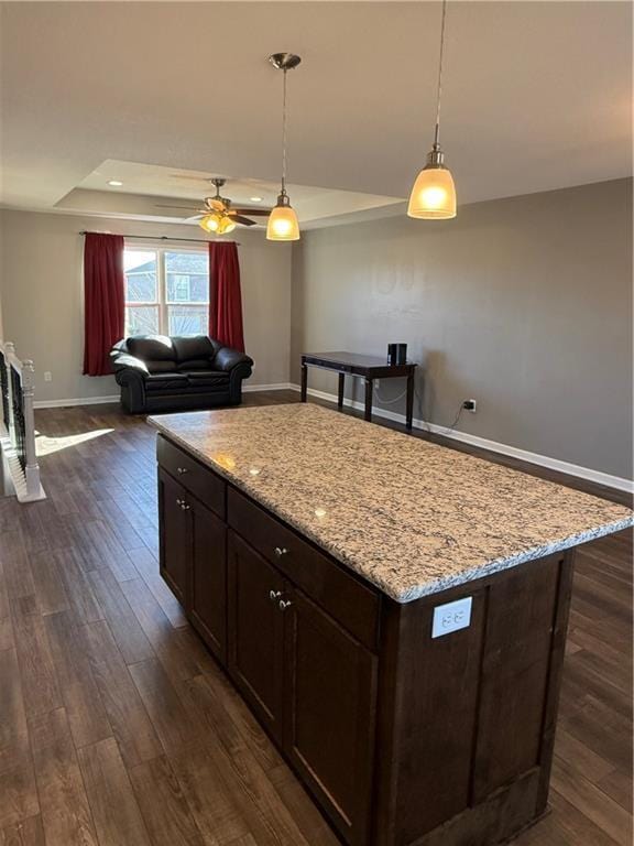 kitchen featuring baseboards, ceiling fan, dark wood-type flooring, decorative light fixtures, and a tray ceiling