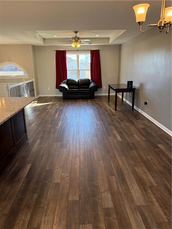 unfurnished living room featuring baseboards, a tray ceiling, dark wood finished floors, and ceiling fan with notable chandelier