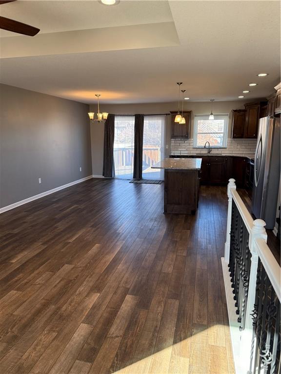 kitchen with dark brown cabinetry, tasteful backsplash, baseboards, a kitchen island, and dark wood-style flooring