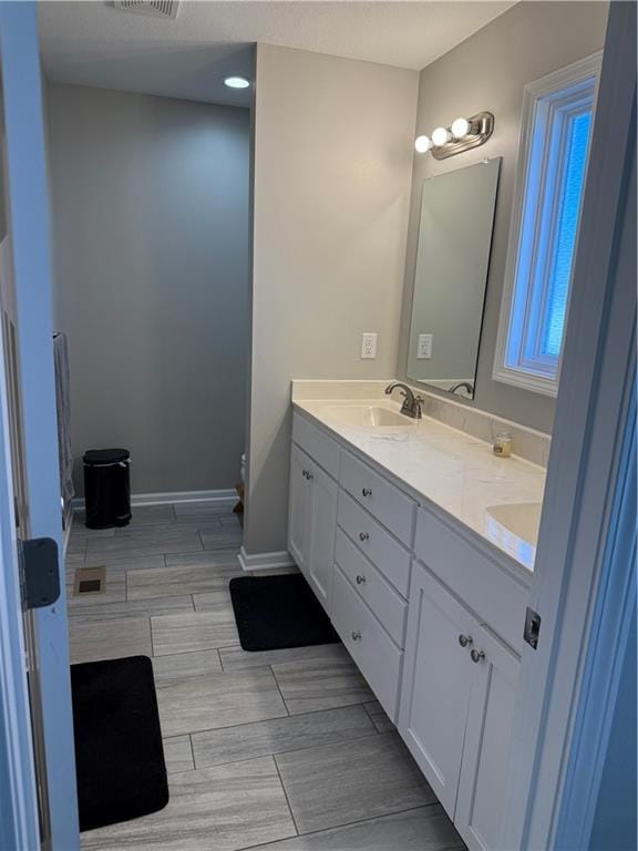 bathroom with a sink, visible vents, baseboards, wood tiled floor, and double vanity