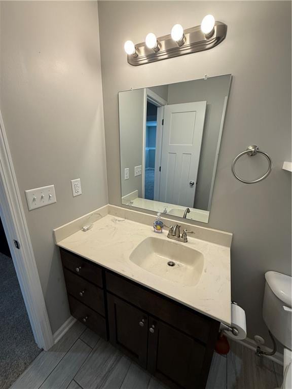 half bathroom featuring toilet, baseboards, and vanity