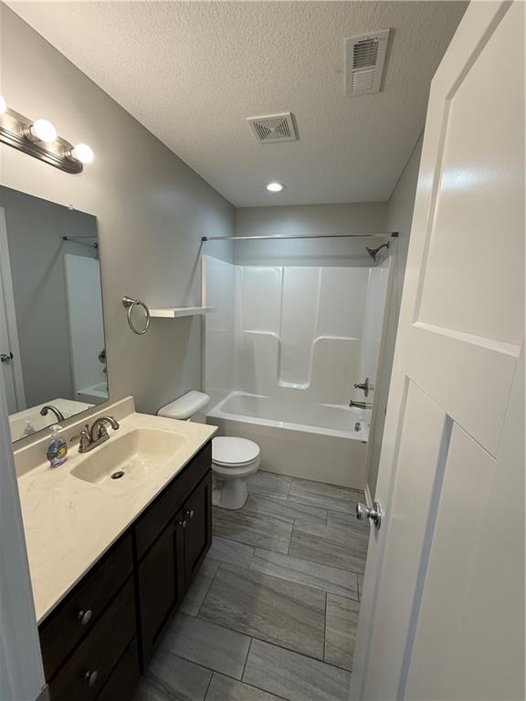 bathroom with visible vents, vanity, toilet, and a textured ceiling