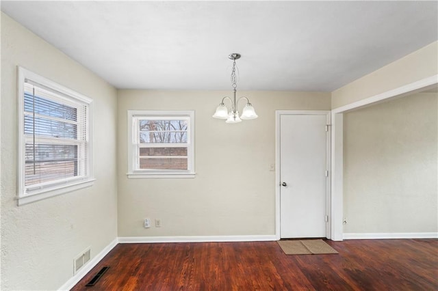 unfurnished dining area featuring a notable chandelier, visible vents, baseboards, and wood finished floors