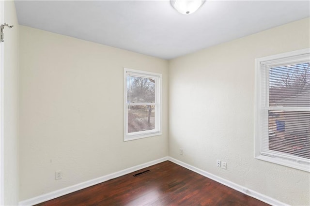 unfurnished room featuring visible vents, baseboards, and dark wood-style floors