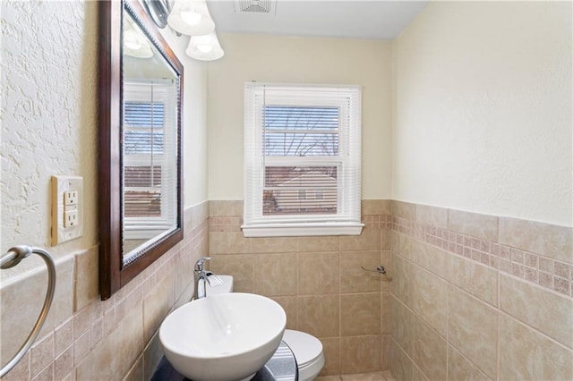 bathroom with a wainscoted wall, plenty of natural light, toilet, and tile walls