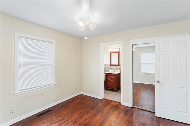 unfurnished bedroom featuring visible vents, dark wood-style floors, baseboards, and connected bathroom