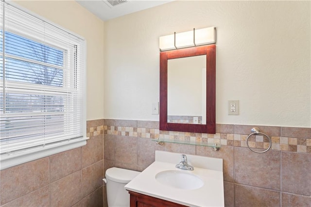 half bathroom with a wainscoted wall, toilet, tile walls, and vanity