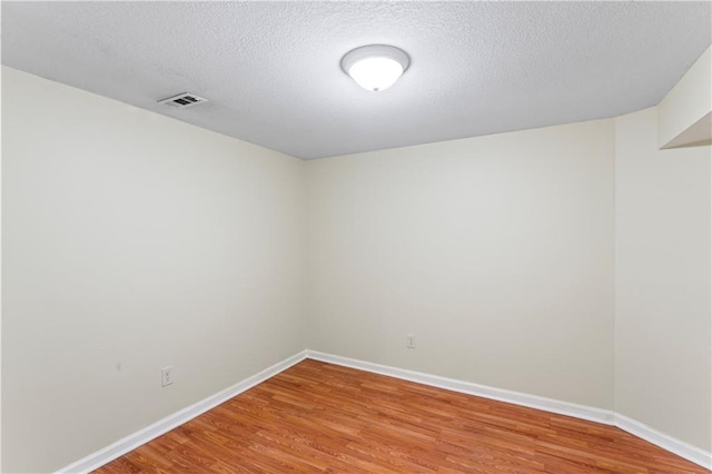 spare room featuring light wood-style flooring, visible vents, baseboards, and a textured ceiling