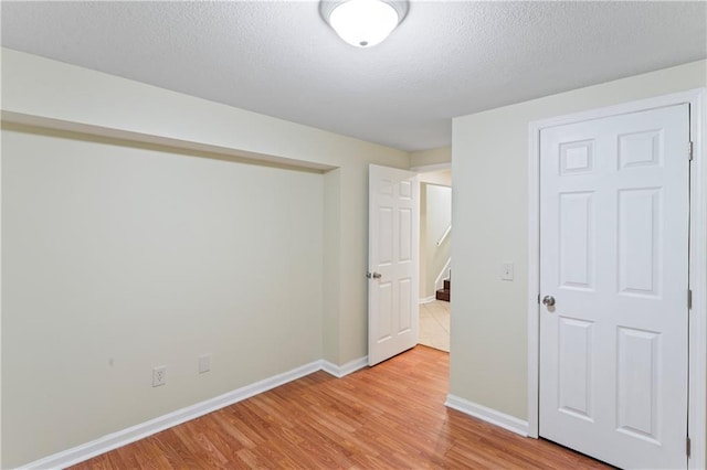 spare room featuring stairs, light wood-style flooring, baseboards, and a textured ceiling