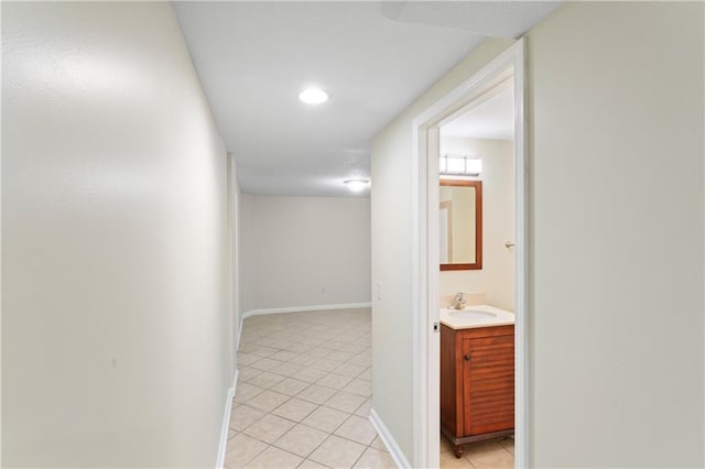 hall featuring light tile patterned flooring, baseboards, and a sink