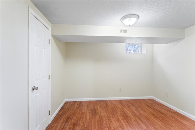 basement featuring visible vents, a textured ceiling, baseboards, and wood finished floors