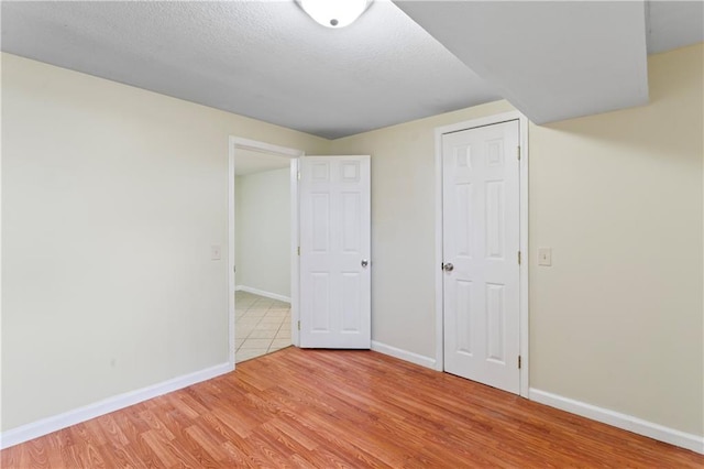 unfurnished bedroom featuring baseboards, a textured ceiling, and light wood-style flooring