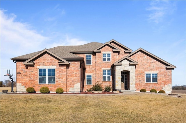 view of front of home featuring a shingled roof, a front yard, stone siding, and brick siding