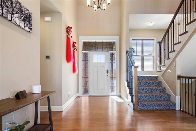 foyer featuring stairs, an inviting chandelier, baseboards, and wood finished floors