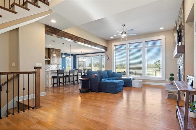 living room featuring a healthy amount of sunlight, light wood-style floors, baseboards, and ceiling fan with notable chandelier