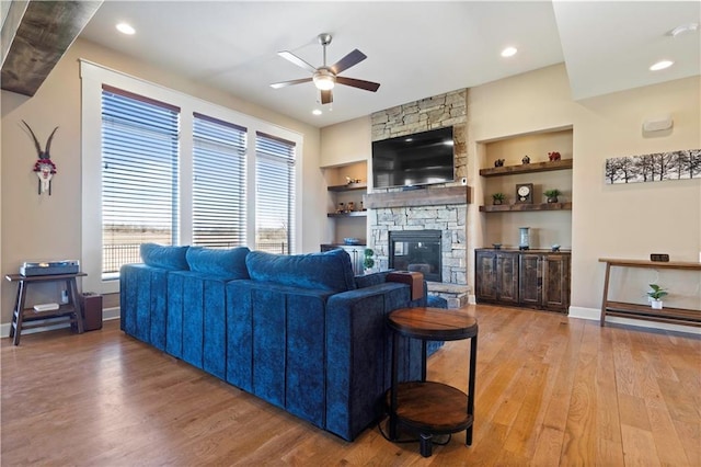 living area featuring ceiling fan, a fireplace, built in features, and light wood-style floors