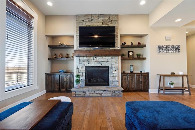 living room with baseboards, built in features, wood finished floors, and a stone fireplace