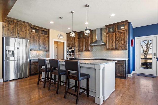 kitchen featuring black electric cooktop, wall chimney exhaust hood, an island with sink, stainless steel fridge, and dark wood finished floors