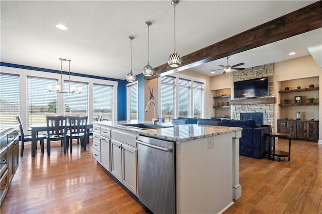 kitchen with a healthy amount of sunlight, a sink, a stone fireplace, and stainless steel dishwasher