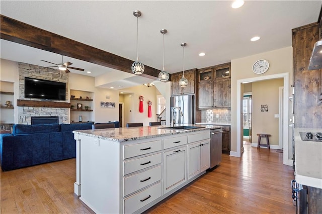 kitchen featuring a fireplace, light wood-style flooring, appliances with stainless steel finishes, a sink, and light stone countertops