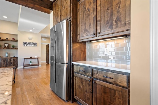 kitchen featuring light wood-style flooring, decorative backsplash, freestanding refrigerator, dark brown cabinetry, and baseboards