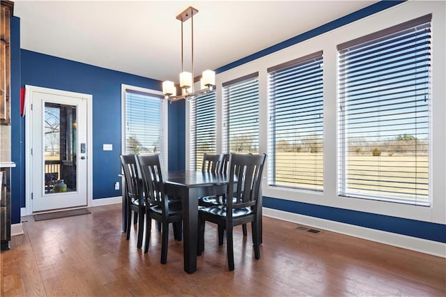 dining space featuring a healthy amount of sunlight, wood finished floors, visible vents, and a notable chandelier