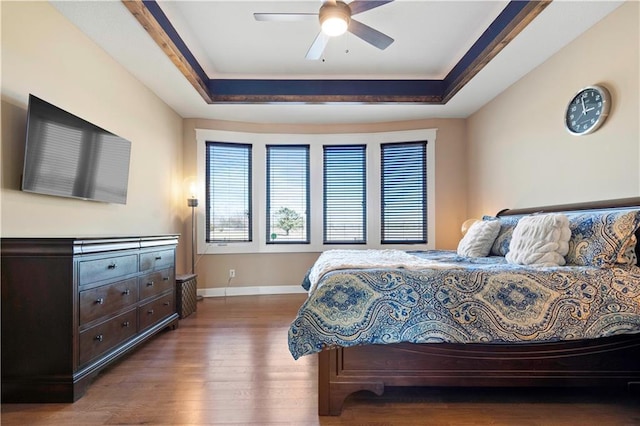 bedroom featuring wood finished floors, a raised ceiling, a ceiling fan, and baseboards